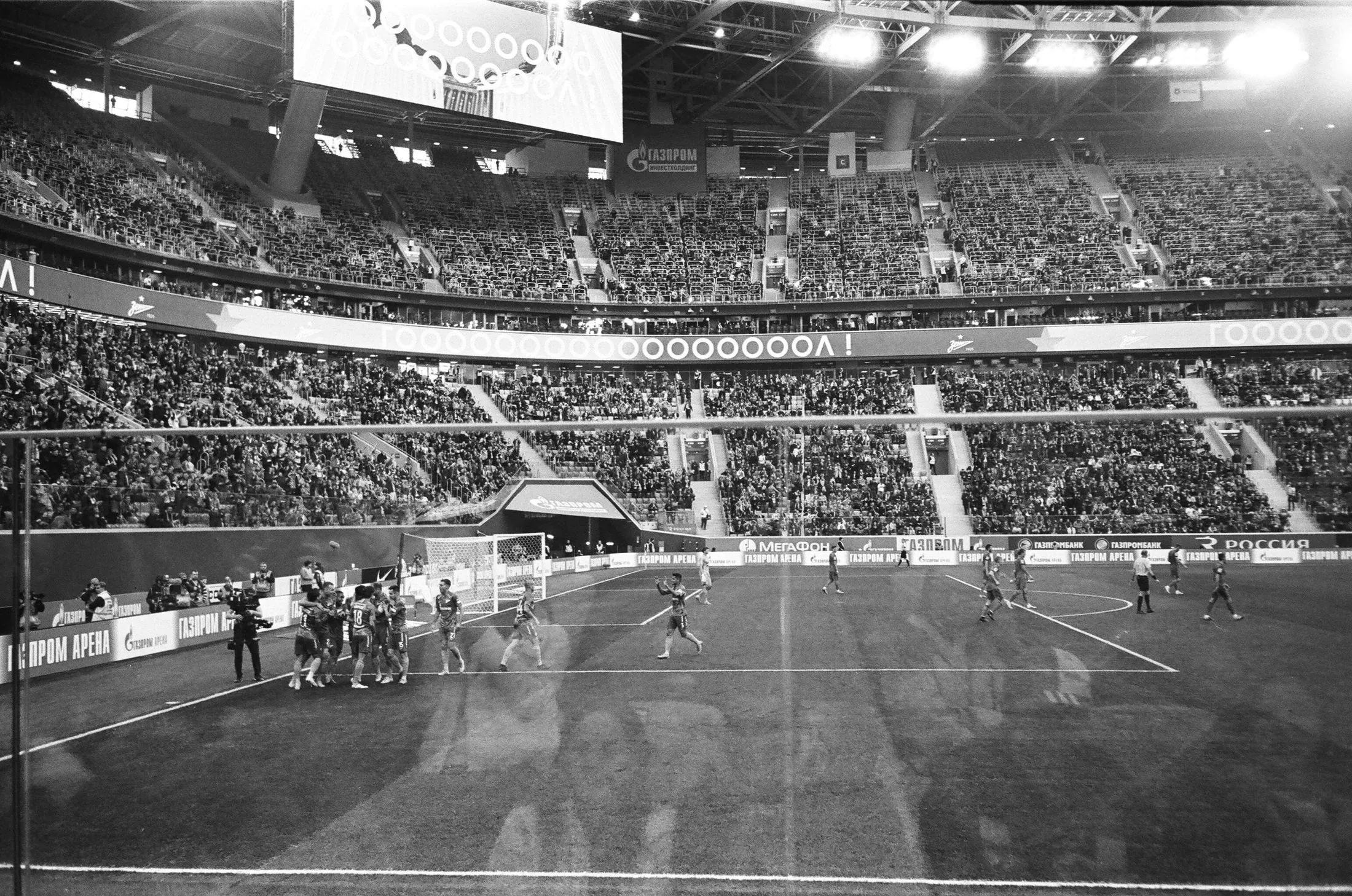 Players celebrating a goal in a floodlit football stadium