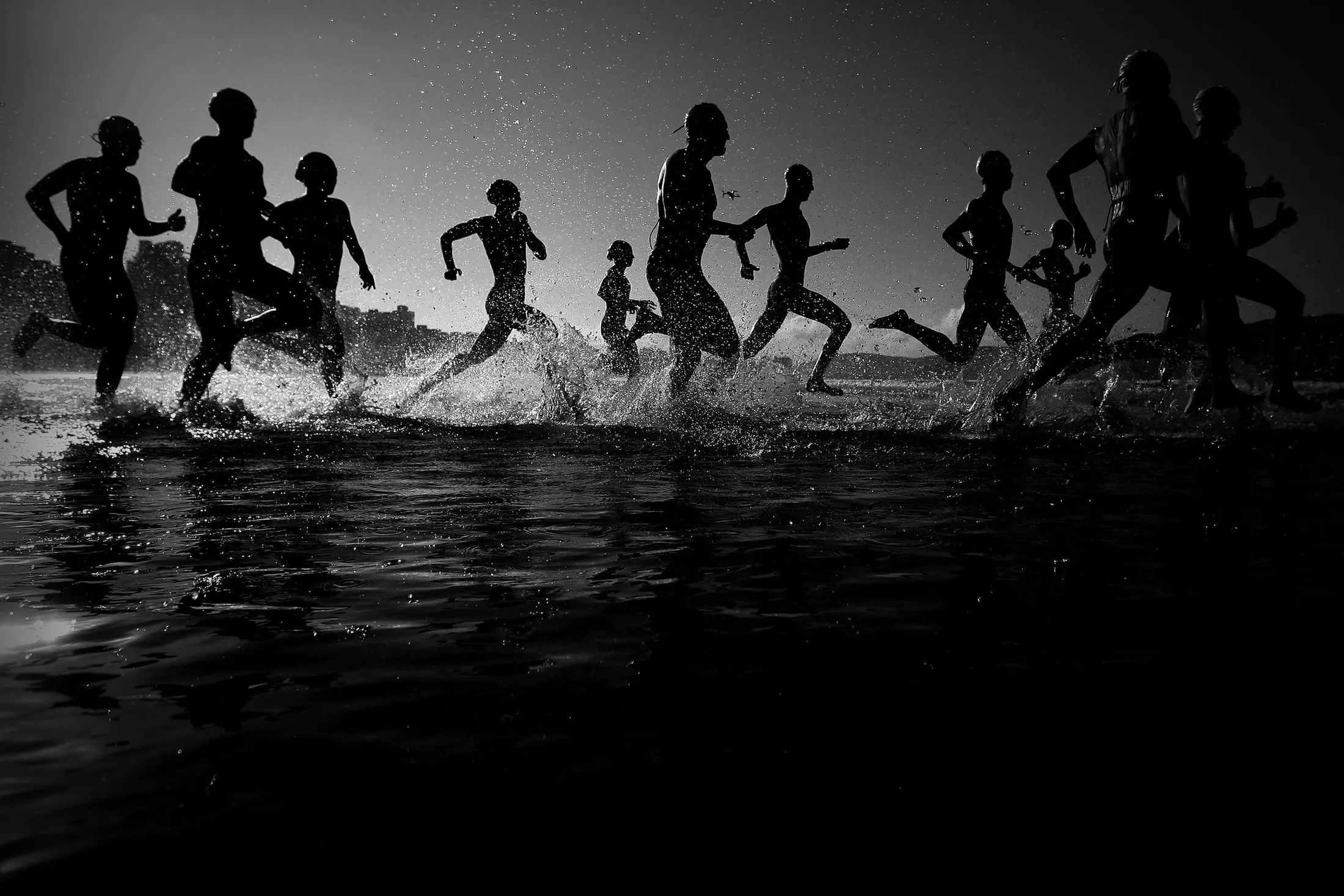 Silhouetted competitors charging into open water at the start of a race