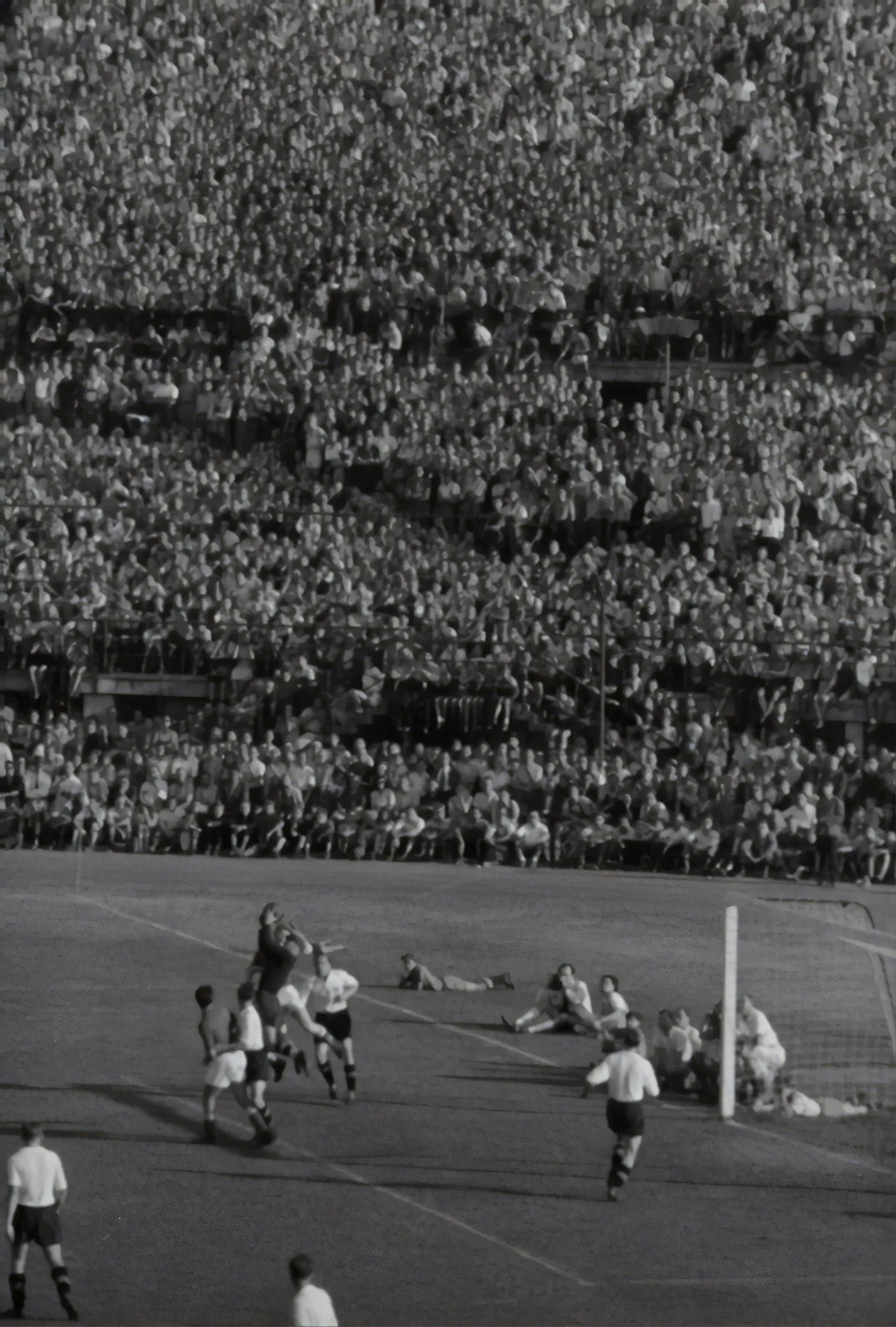 A packed mid-century football terrace, thousands of spectators watching a match